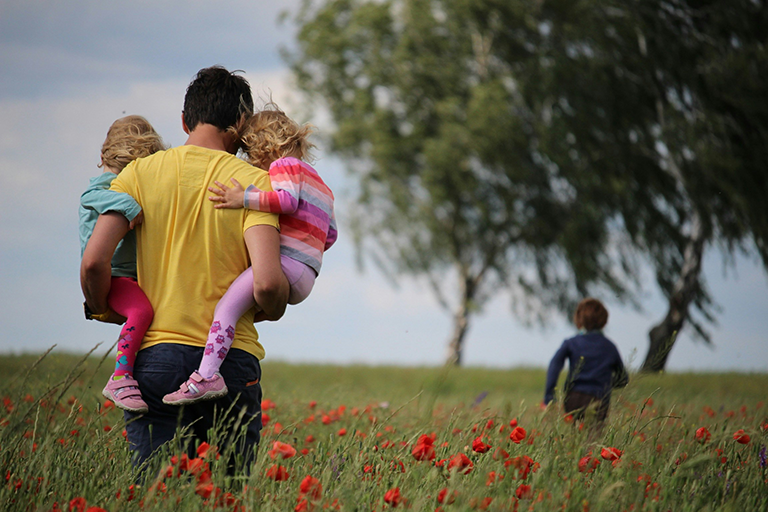 Ein Mann spaziert mit drei Kindern über eine Mohnblumenwiese