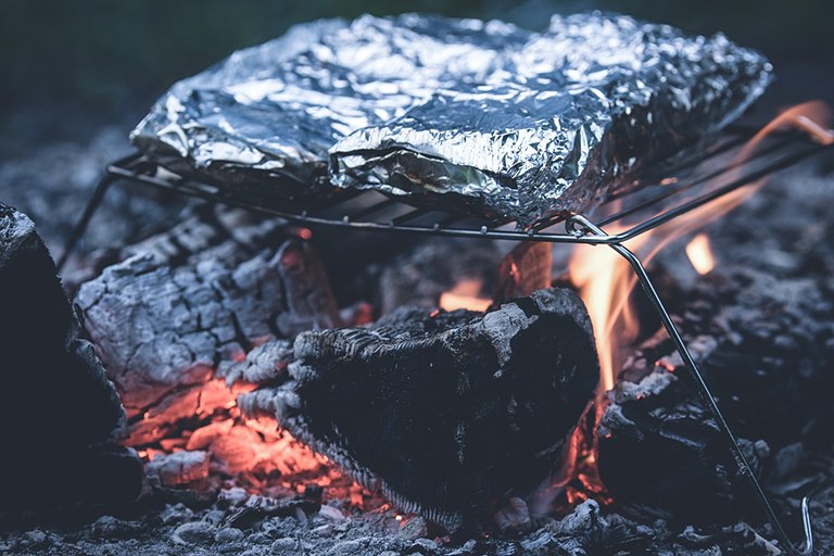 Essen in Alufolie verpackt liegt auf einem Griller