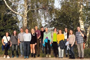 Gruppenfoto mit 13 Personen, die vor grünen Bäumen stehen