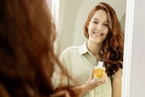 Junge Frau mit glänzendem Haar und Produkt in der Hand schaut in den Spiegel