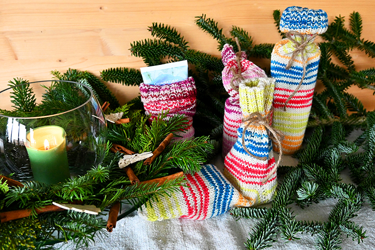 Vier in Socken verpackte Geschenke stehen vor Tannenzweigen und einer Kerze